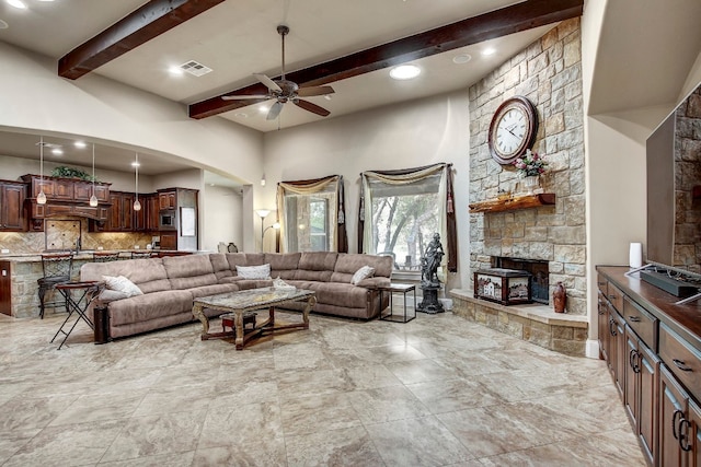 living room featuring ceiling fan, beamed ceiling, and a stone fireplace