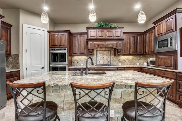 kitchen featuring appliances with stainless steel finishes, a center island with sink, sink, and decorative light fixtures