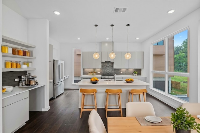 kitchen featuring appliances with stainless steel finishes, tasteful backsplash, an island with sink, a kitchen breakfast bar, and hanging light fixtures