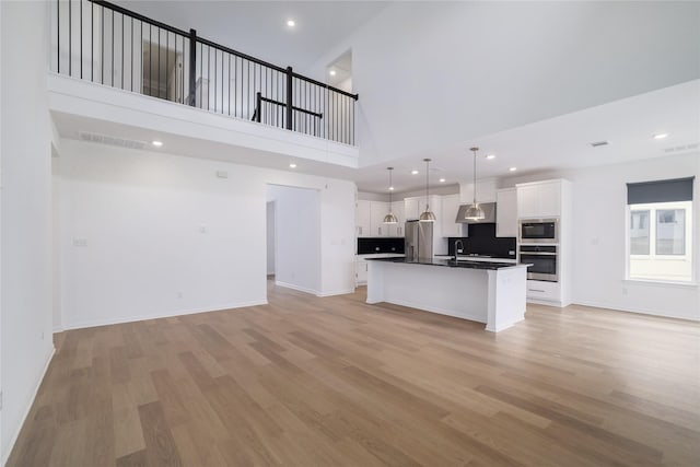 kitchen featuring a high ceiling, white cabinets, appliances with stainless steel finishes, hanging light fixtures, and a center island with sink