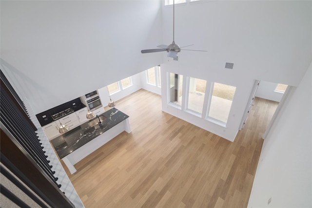 unfurnished living room with ceiling fan, light hardwood / wood-style flooring, and a towering ceiling