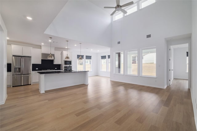 kitchen featuring pendant lighting, a towering ceiling, a kitchen island with sink, stainless steel appliances, and white cabinets