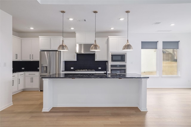 kitchen featuring appliances with stainless steel finishes, white cabinets, dark stone counters, and an island with sink