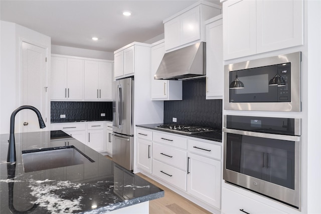 kitchen with white cabinets, stainless steel appliances, wall chimney exhaust hood, and dark stone countertops