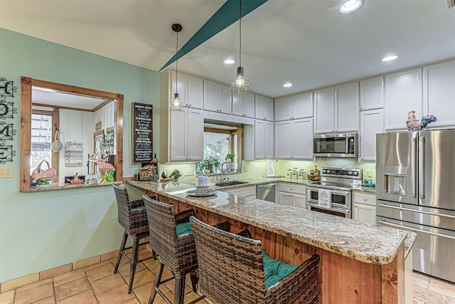 kitchen with appliances with stainless steel finishes, light stone counters, white cabinets, kitchen peninsula, and sink