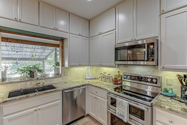 kitchen featuring tasteful backsplash, sink, white cabinetry, stainless steel appliances, and light stone countertops