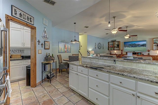 kitchen featuring light stone counters, white cabinets, ceiling fan, lofted ceiling, and decorative light fixtures