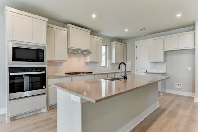 kitchen with a center island with sink, white cabinets, sink, light hardwood / wood-style flooring, and appliances with stainless steel finishes