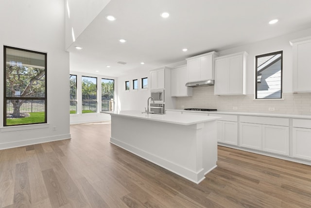 kitchen with sink, white cabinetry, black gas cooktop, a center island with sink, and built in microwave