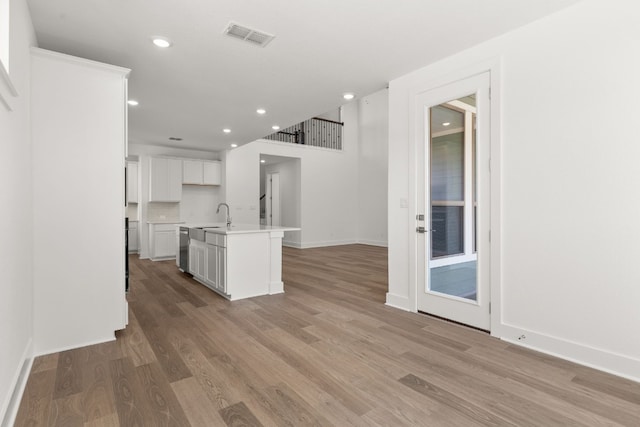 kitchen featuring sink, a kitchen island with sink, white cabinetry, tasteful backsplash, and light hardwood / wood-style floors