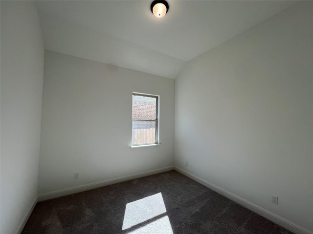 spare room featuring dark carpet and vaulted ceiling