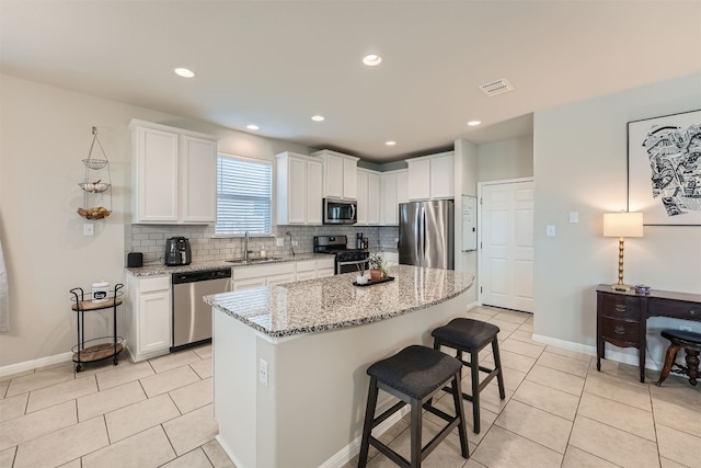 kitchen with white cabinets, sink, a kitchen island, appliances with stainless steel finishes, and light stone countertops