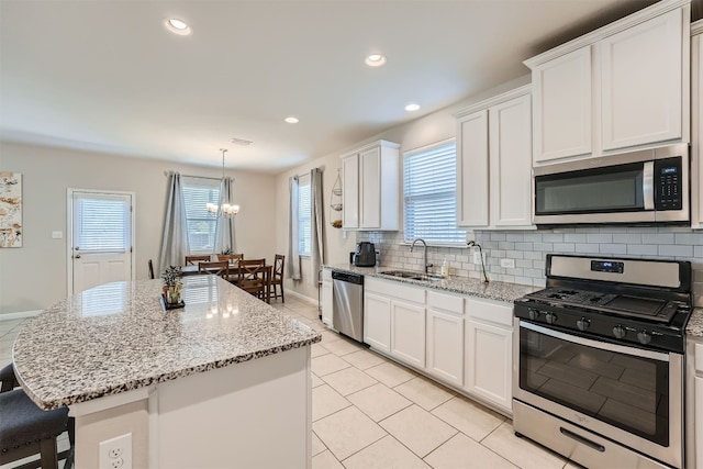 kitchen with white cabinets, sink, a kitchen island, stainless steel appliances, and a notable chandelier