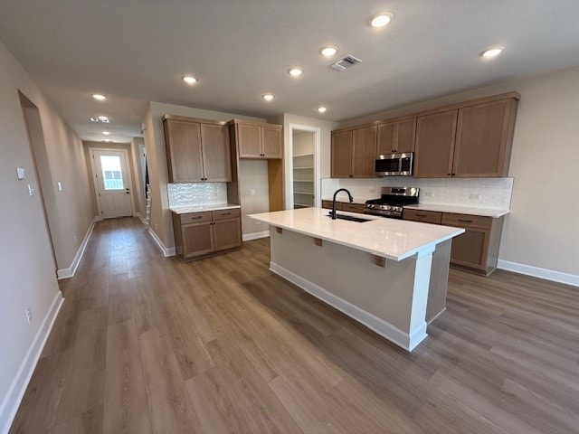 kitchen featuring hardwood / wood-style flooring, backsplash, stainless steel appliances, and an island with sink