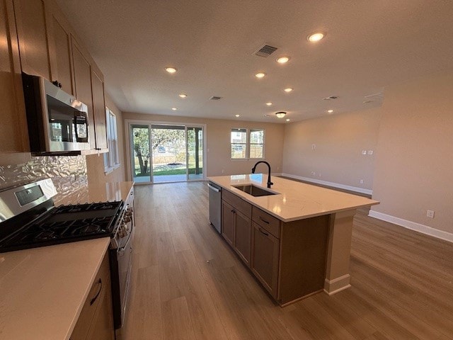 kitchen featuring sink, backsplash, hardwood / wood-style floors, a kitchen island with sink, and appliances with stainless steel finishes