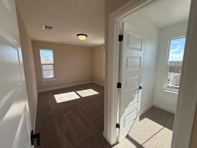 hallway featuring dark colored carpet and a wealth of natural light