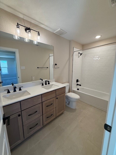 full bathroom with tiled shower / bath, vanity, a textured ceiling, and toilet