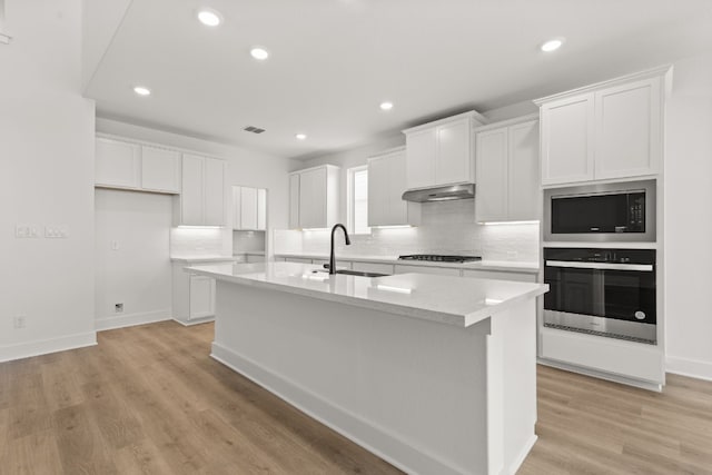 kitchen featuring built in microwave, an island with sink, white cabinets, and oven