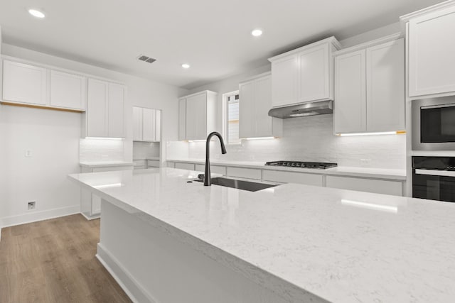 kitchen featuring sink, appliances with stainless steel finishes, white cabinetry, backsplash, and light stone countertops