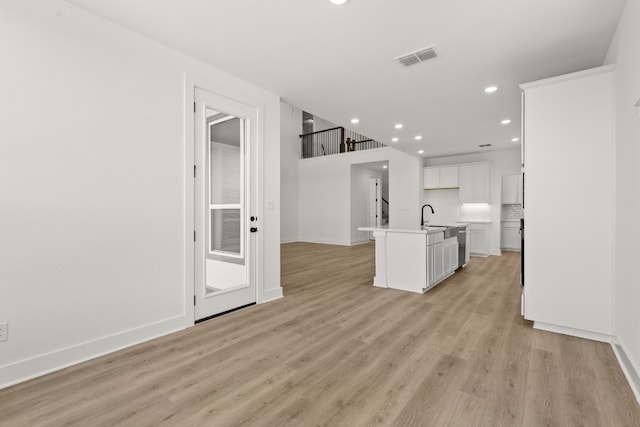 interior space featuring a kitchen island with sink, sink, light hardwood / wood-style flooring, and white cabinets