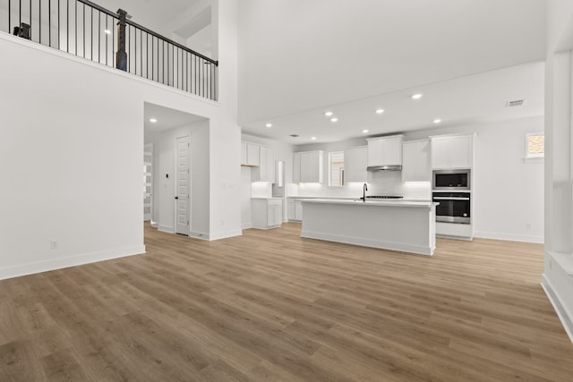 unfurnished living room featuring wood-type flooring, sink, and a high ceiling