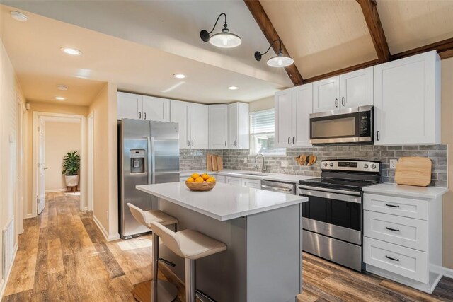 kitchen featuring beam ceiling, white cabinetry, appliances with stainless steel finishes, a center island, and light hardwood / wood-style floors