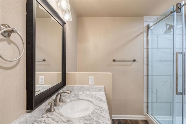full bath featuring vanity, a stall shower, baseboards, and wood finished floors