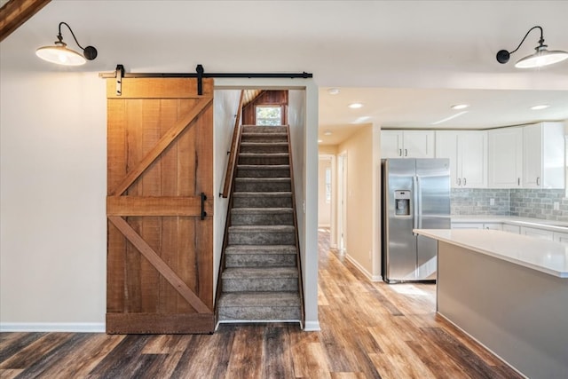 kitchen with tasteful backsplash, stainless steel refrigerator with ice dispenser, white cabinetry, a barn door, and hardwood / wood-style floors