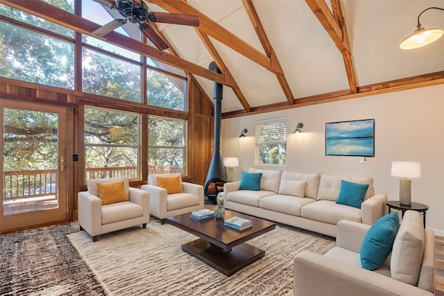 living room featuring ceiling fan, beamed ceiling, a wood stove, and high vaulted ceiling