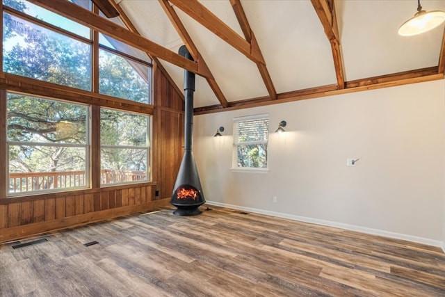 unfurnished room with high vaulted ceiling, a wood stove, beam ceiling, and hardwood / wood-style flooring