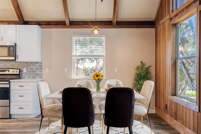 dining space with light wood-type flooring, wood walls, and beam ceiling