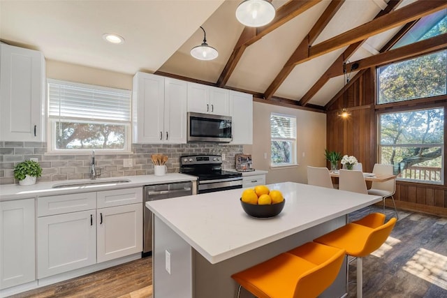 kitchen with a sink, lofted ceiling with beams, wood finished floors, a breakfast bar, and stainless steel appliances