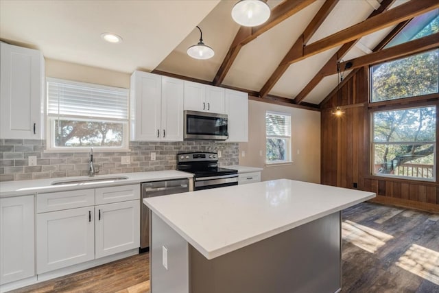 kitchen with appliances with stainless steel finishes, vaulted ceiling with beams, white cabinetry, and sink