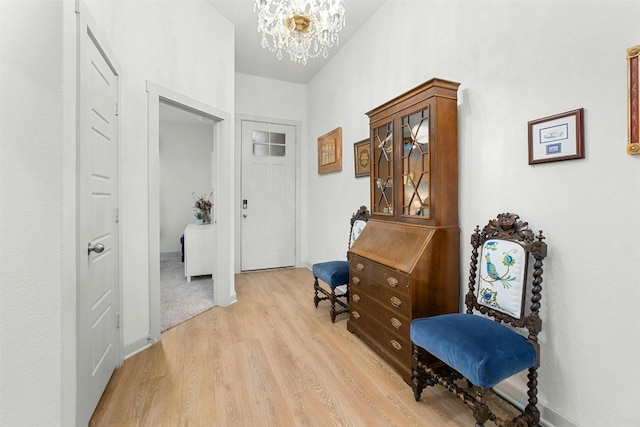 corridor featuring light wood-style floors, a notable chandelier, and baseboards