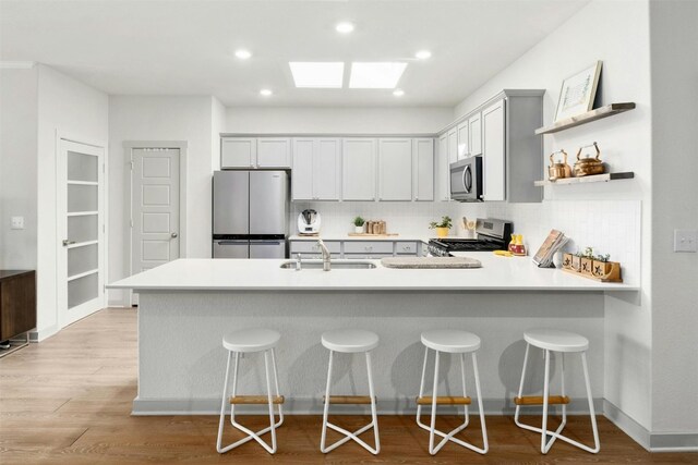 kitchen featuring a breakfast bar area, a peninsula, light countertops, appliances with stainless steel finishes, and open shelves