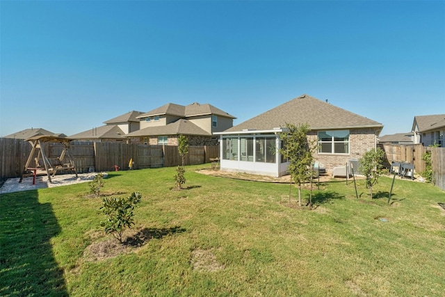 rear view of house with roof with shingles, a sunroom, a patio area, a fenced backyard, and a yard
