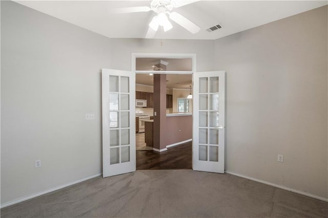 spare room featuring french doors, ceiling fan, and dark colored carpet