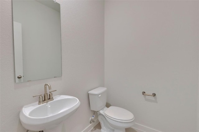 half bath featuring toilet, baseboards, and a sink