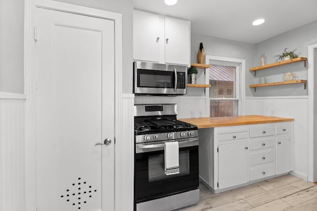 kitchen with appliances with stainless steel finishes, butcher block countertops, light wood-type flooring, and white cabinets