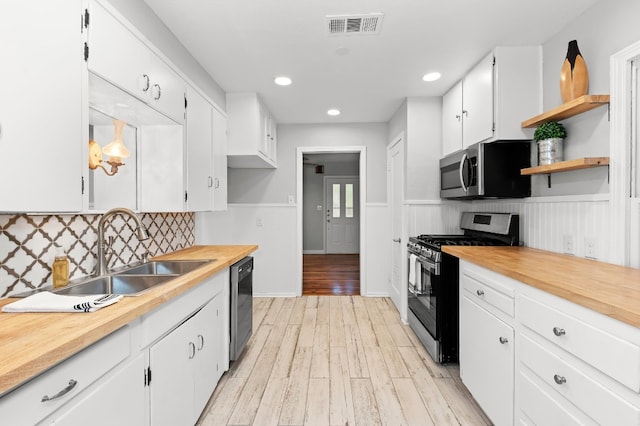 kitchen with tasteful backsplash, sink, white cabinets, light hardwood / wood-style flooring, and stainless steel appliances