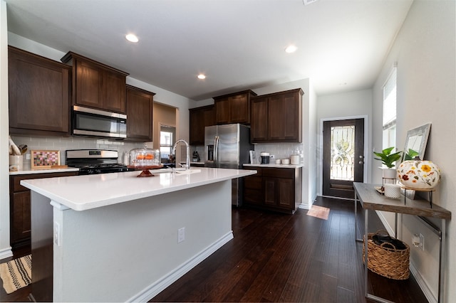 kitchen featuring decorative backsplash, dark brown cabinets, dark wood-type flooring, stainless steel appliances, and an island with sink