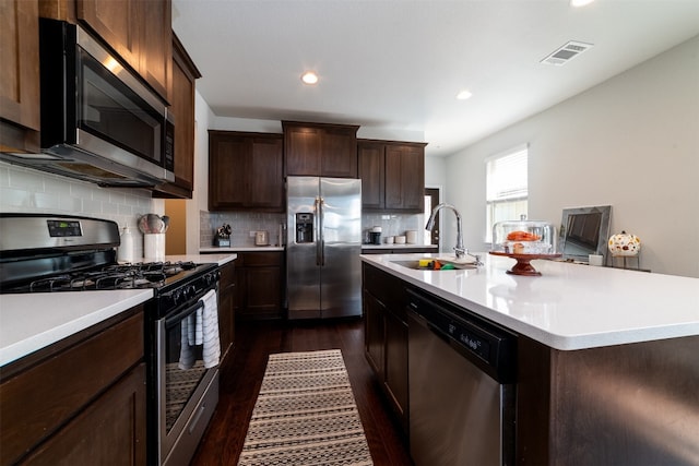 kitchen featuring decorative backsplash, a kitchen island with sink, dark hardwood / wood-style floors, stainless steel appliances, and sink