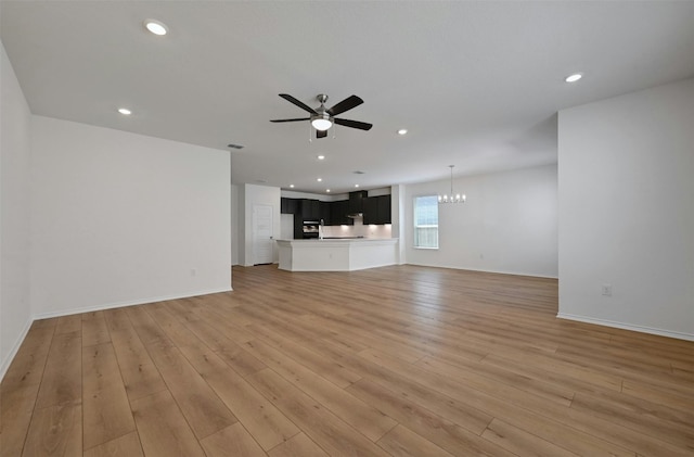 unfurnished living room featuring ceiling fan with notable chandelier and light hardwood / wood-style floors