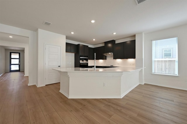 kitchen with double oven, light wood-type flooring, backsplash, and sink