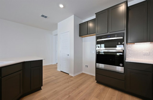 kitchen with decorative backsplash, stainless steel double oven, and light hardwood / wood-style flooring