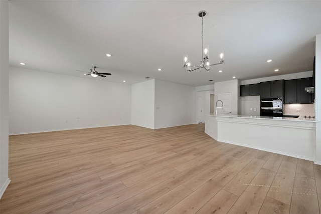 unfurnished living room with ceiling fan with notable chandelier and light hardwood / wood-style flooring