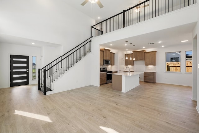 kitchen with a center island with sink, stainless steel appliances, a high ceiling, and light hardwood / wood-style floors