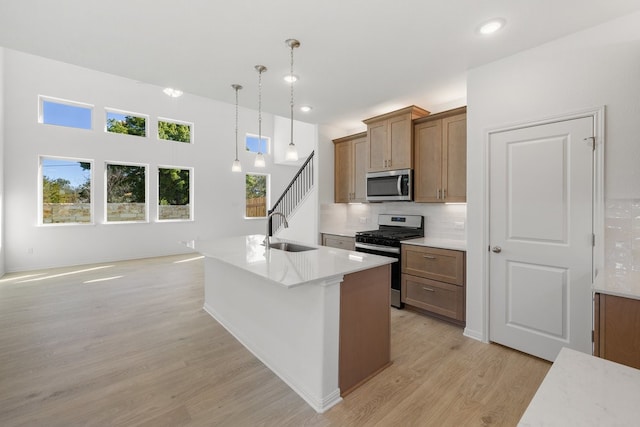 kitchen with appliances with stainless steel finishes, sink, decorative light fixtures, light hardwood / wood-style floors, and an island with sink