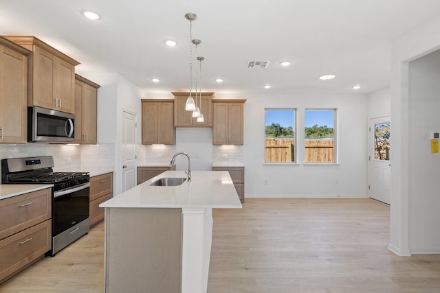 kitchen featuring sink, light wood-type flooring, stainless steel appliances, and an island with sink