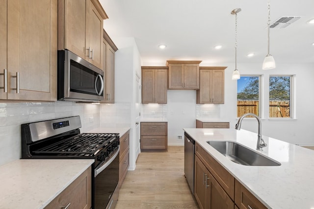 kitchen featuring light stone countertops, sink, stainless steel appliances, pendant lighting, and light hardwood / wood-style floors